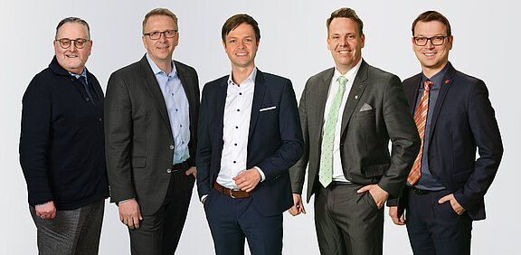 Hauptverwaltungsbeamte der KAG Freiraum Ruppiner Land Fünf Hauptverwaltungsbeamten der KAG Freiraum Ruppiner Land stehen nebeneinander vor einem neutralen Hintergrund. Sie tragen formelle Kleidung und lächeln. Jeder Mann hat einen unterschiedlichen Stil, von business-casual bis zum Anzug. Die Gruppe strahlt Professionalität und Selbstbewusstsein aus.